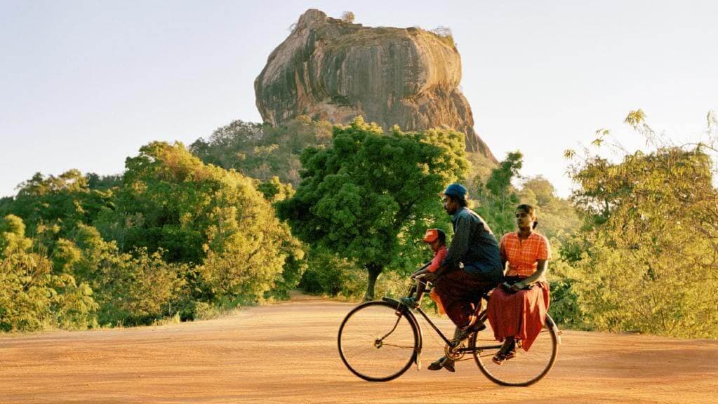 Una familia local en bicicleta frente a la roca de Sigiriya en Sri Lanka