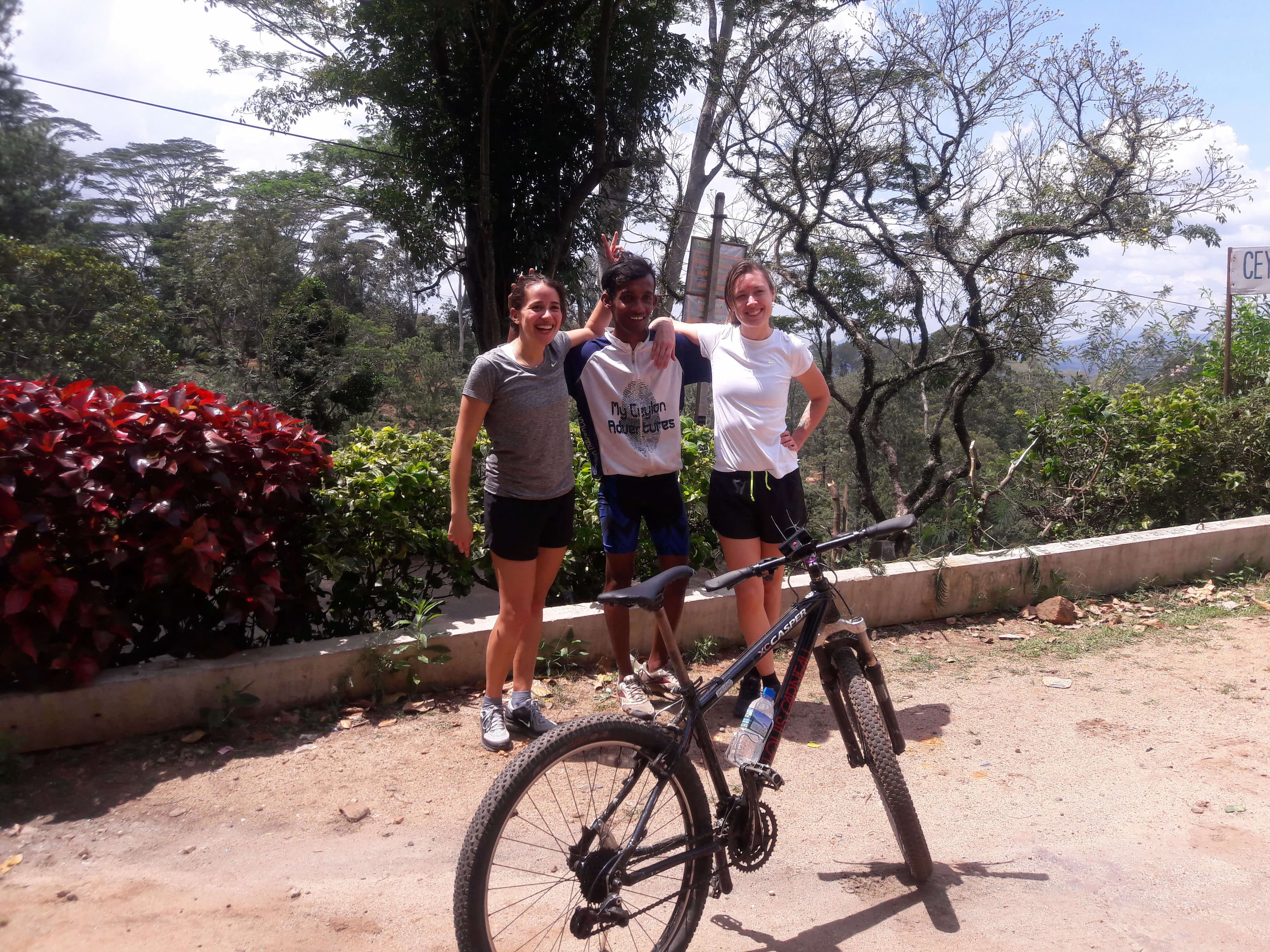 两名游客在斯里兰卡康提茶园骑自行车时与导游合影