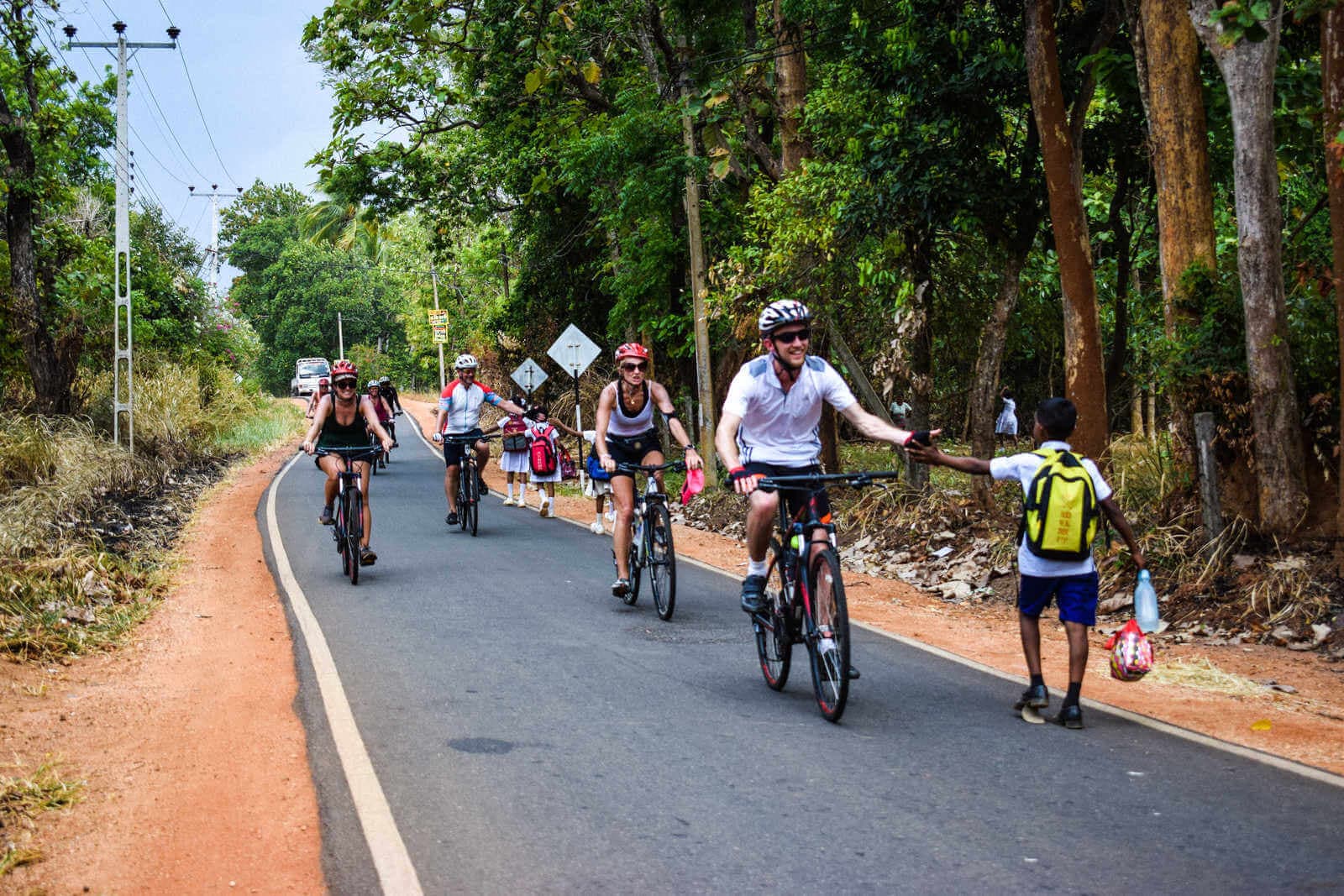 Туристы встречают школьника во время велотура по сельской местности Мириссы на Шри-Ланке.