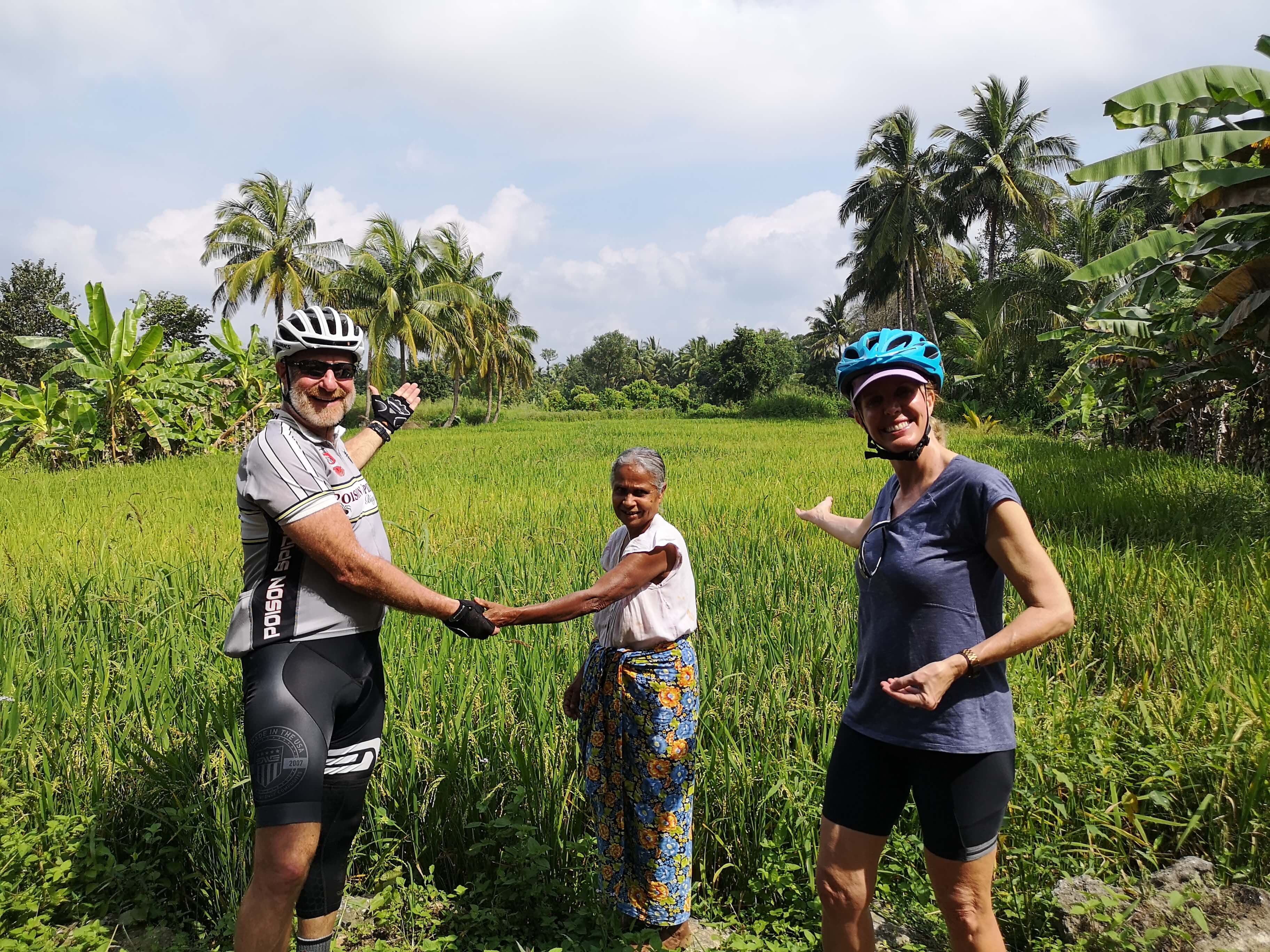 Фотография велосипедистов, наблюдающих за загородным рисовым полем и встречающих дружелюбных местных жителей на Шри-Ланке.