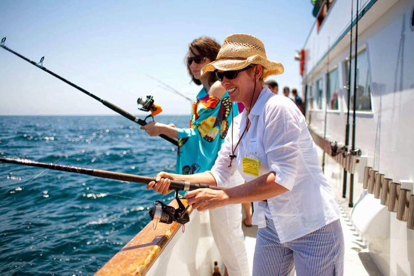 Una mujer turista pescando un pez con la cara sonriente y otra mujer lo mira
