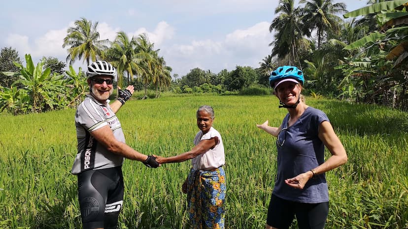 两名骑自行车的人与当地农夫在斯里兰卡的稻田里。